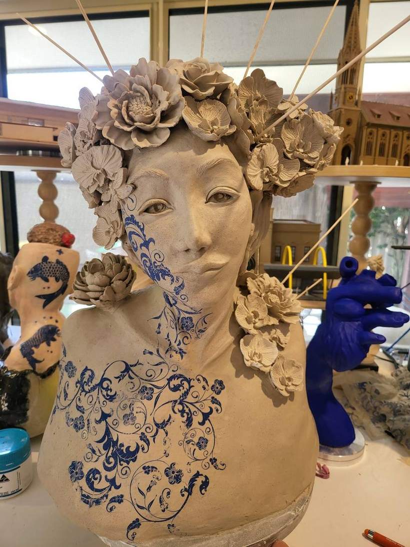 Ceramic bust with a floral crown and hand-painted blue willow-pattern florals across the shoulders and chest, unfired stoneware