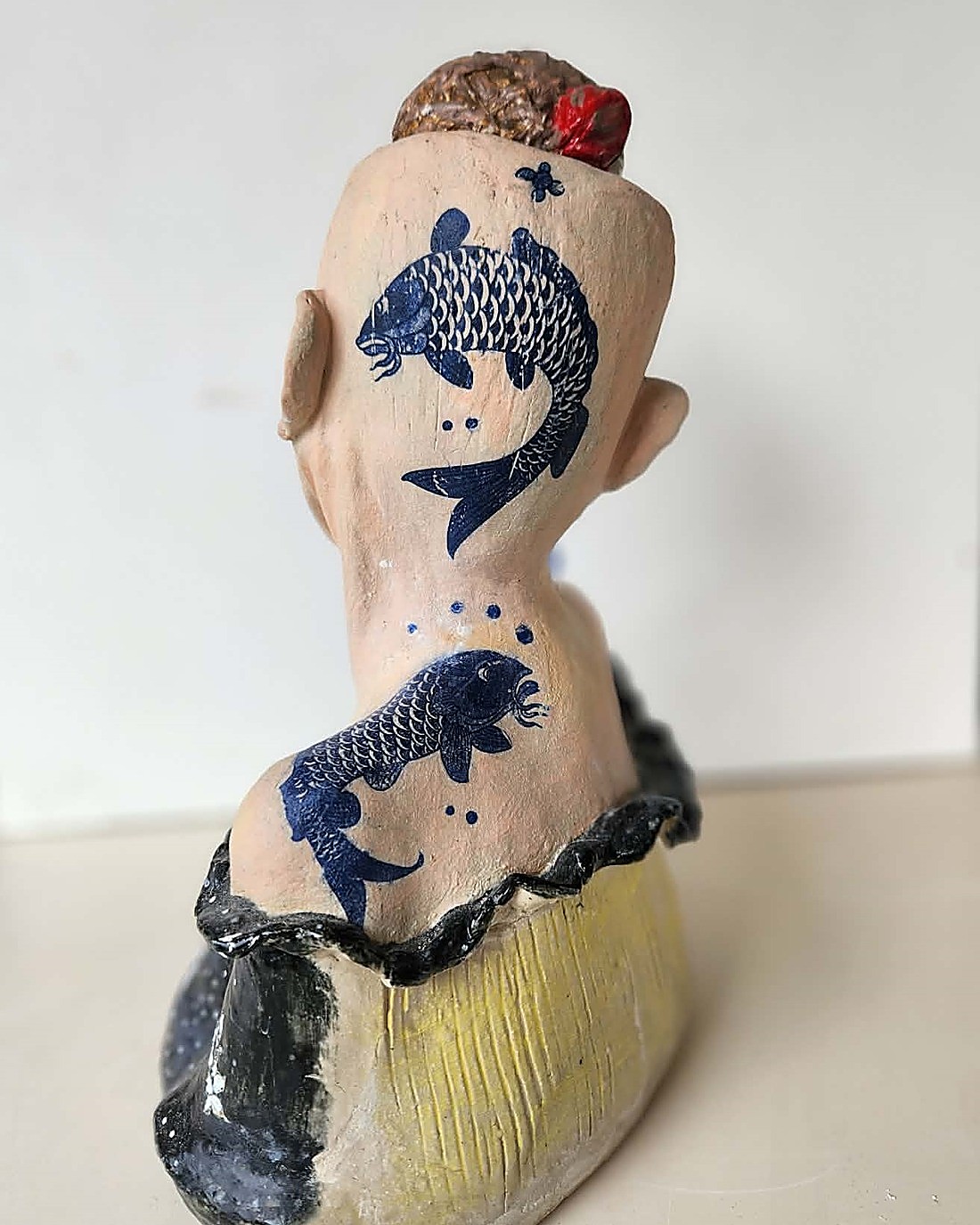 The same glazed portrait bust, back view — two dark blue koi-fish glaze transfers running down the back of the head to the upper back, a small hair bun with a red accent at the crown, and the black dress at the base
