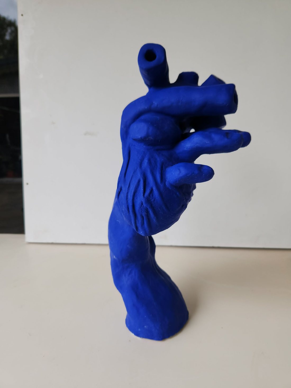 The same hand-and-heart sculpture finished in a flat, intense ultramarine blue acrylic, shown from the side