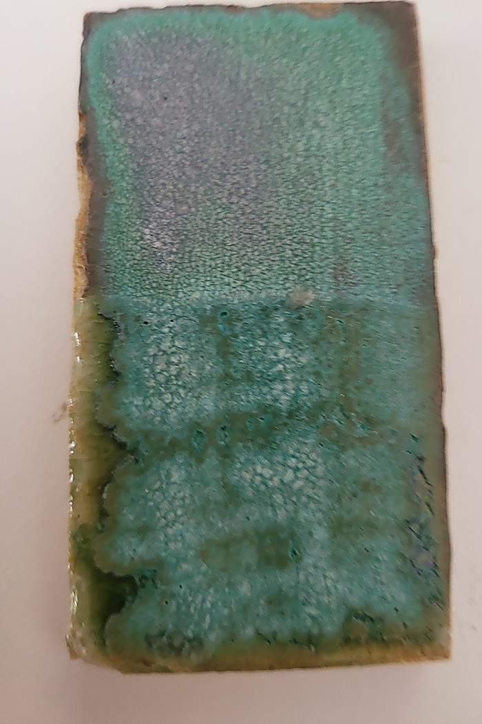 A test tile in Weathered Green, the lower half brighter and glossier where clear glaze has been laid over the top, breaking into a crawled turquoise