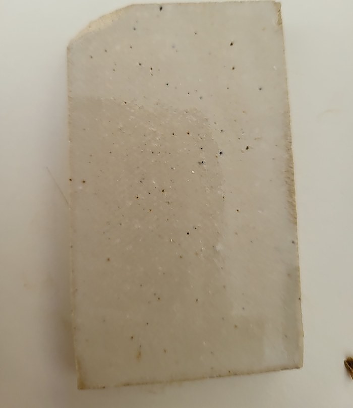 A test tile glazed overall in Milky Gloss — a smooth, faintly blue-white surface with a soft sheen