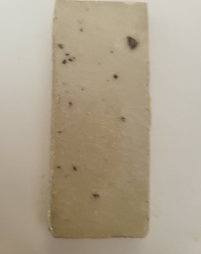 A test tile in Clear Selsor — the glaze transparent, so the dark iron speckles in the clay body show through