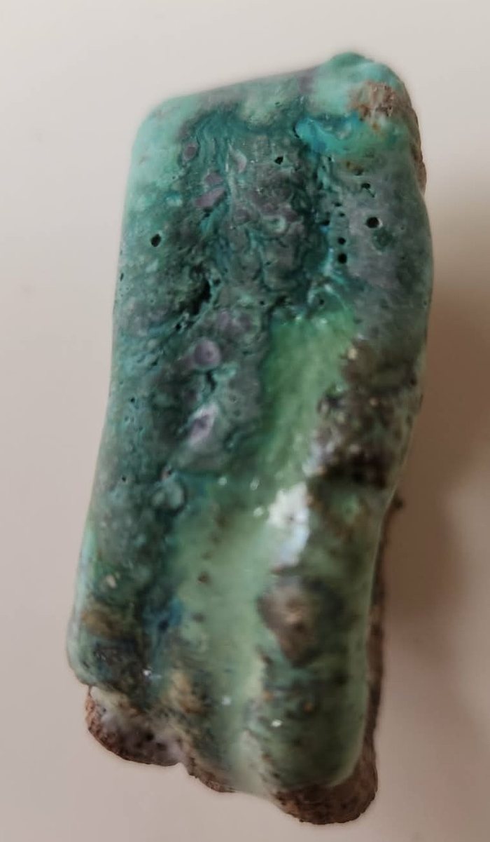 A test tile glazed overall in Weathered Green, the top layered further with Chun Seafoam and Selsor White — a pale seafoam surface breaking into a dense mottled grey-green texture with fine dark speckling, on Raku clay