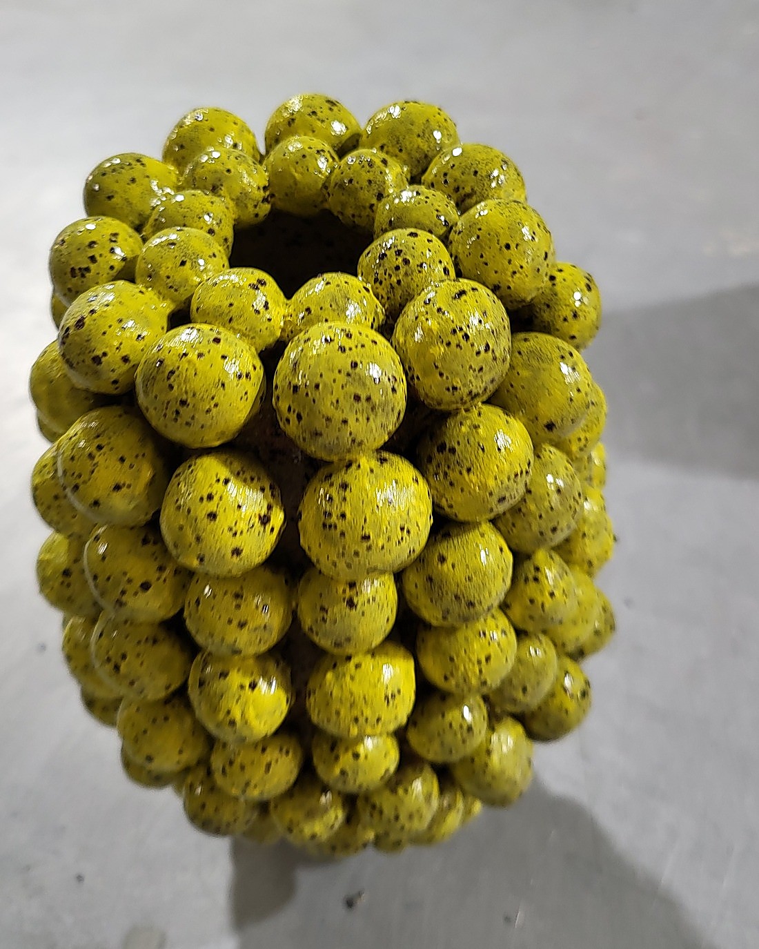The same clay-sphere vessel after firing — the daffodil yellow underglaze now glossy and speckled with fine dark flecks