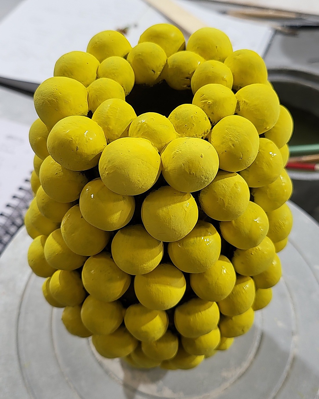 A vessel built entirely from rows of hand-formed clay spheres, brushed all over with matte daffodil yellow underglaze before firing, on the studio wheel