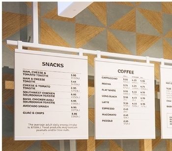 White menu boards for snacks and coffee hanging from a rail in front of a patterned timber backdrop