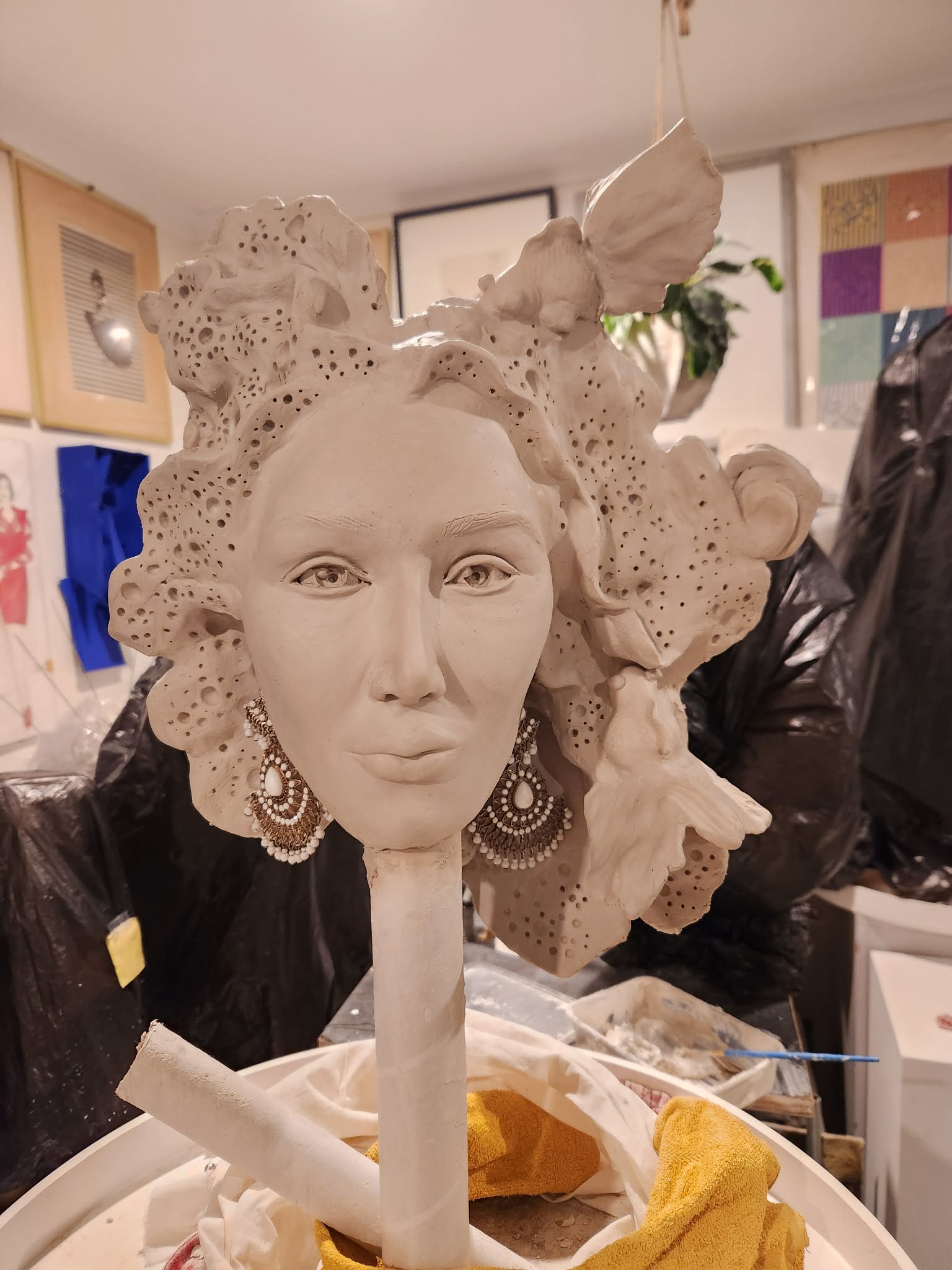 The Fashion Designer&rsquo;s head in greenware on its stand &mdash; a calm three-quarter face framed by broad coral fronds pierced all over with holes, a long beaded chandelier earring at one ear