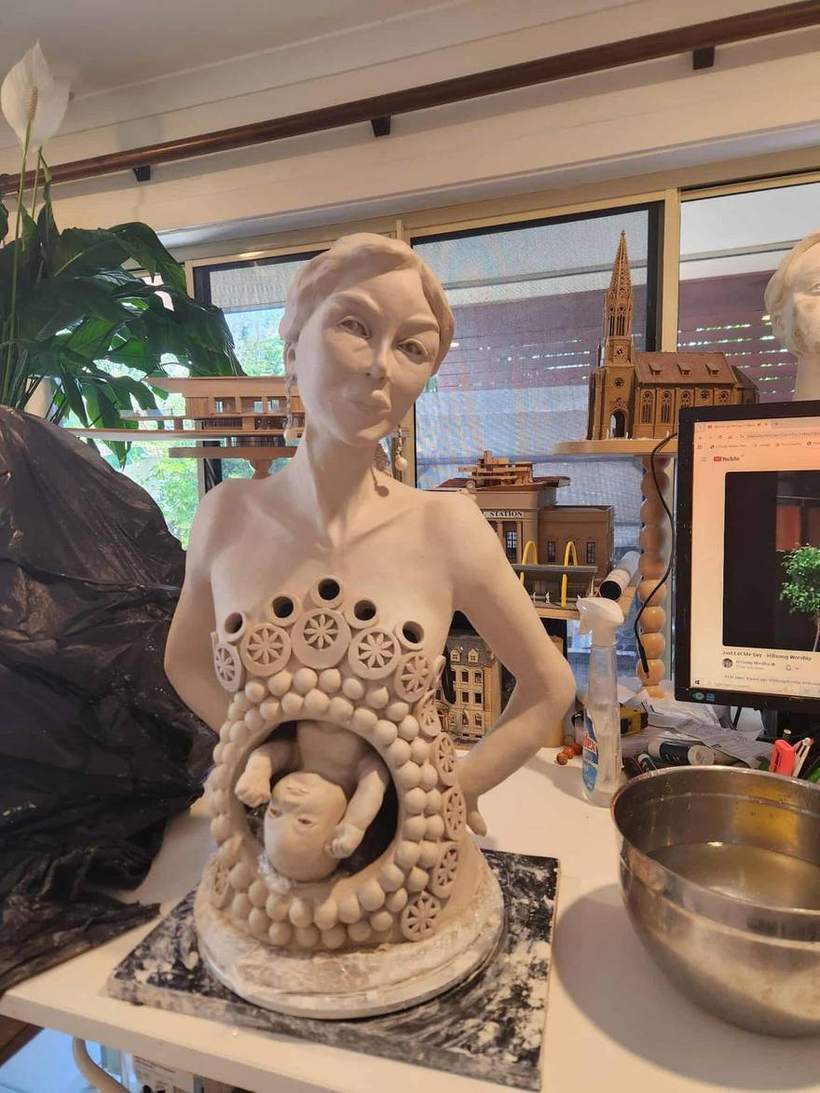 Ceramic sculpture of a mother figure with small openings across the body and figures nestled in the hair