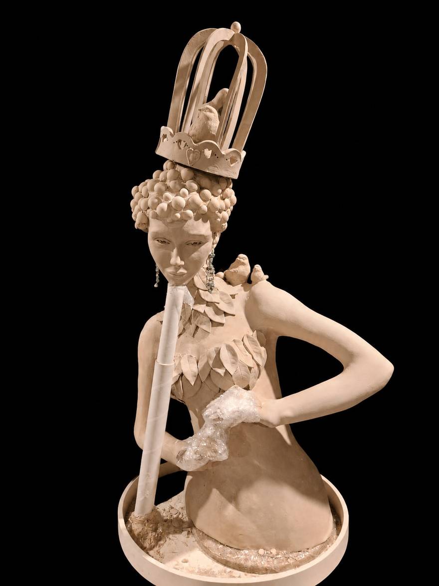 The Wildlife Rehabilitator in greenware &mdash; a birdcage with a bird inside rising from a heart-pierced crown, hair built from small clay balls, a collar of layered leaves and two small birds perched on her shoulder