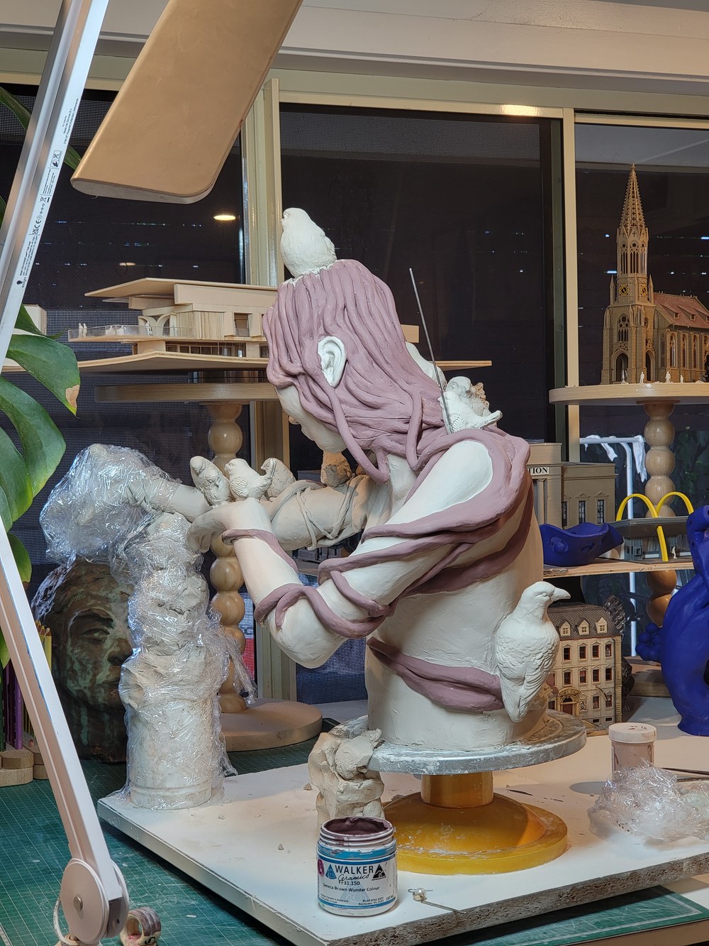 The same view once the surface was painted &mdash; the coiled hair in soft pink and lilac falling across the back, white birds perched along the shoulder and arm, the sculpture standing on its turntable in the studio