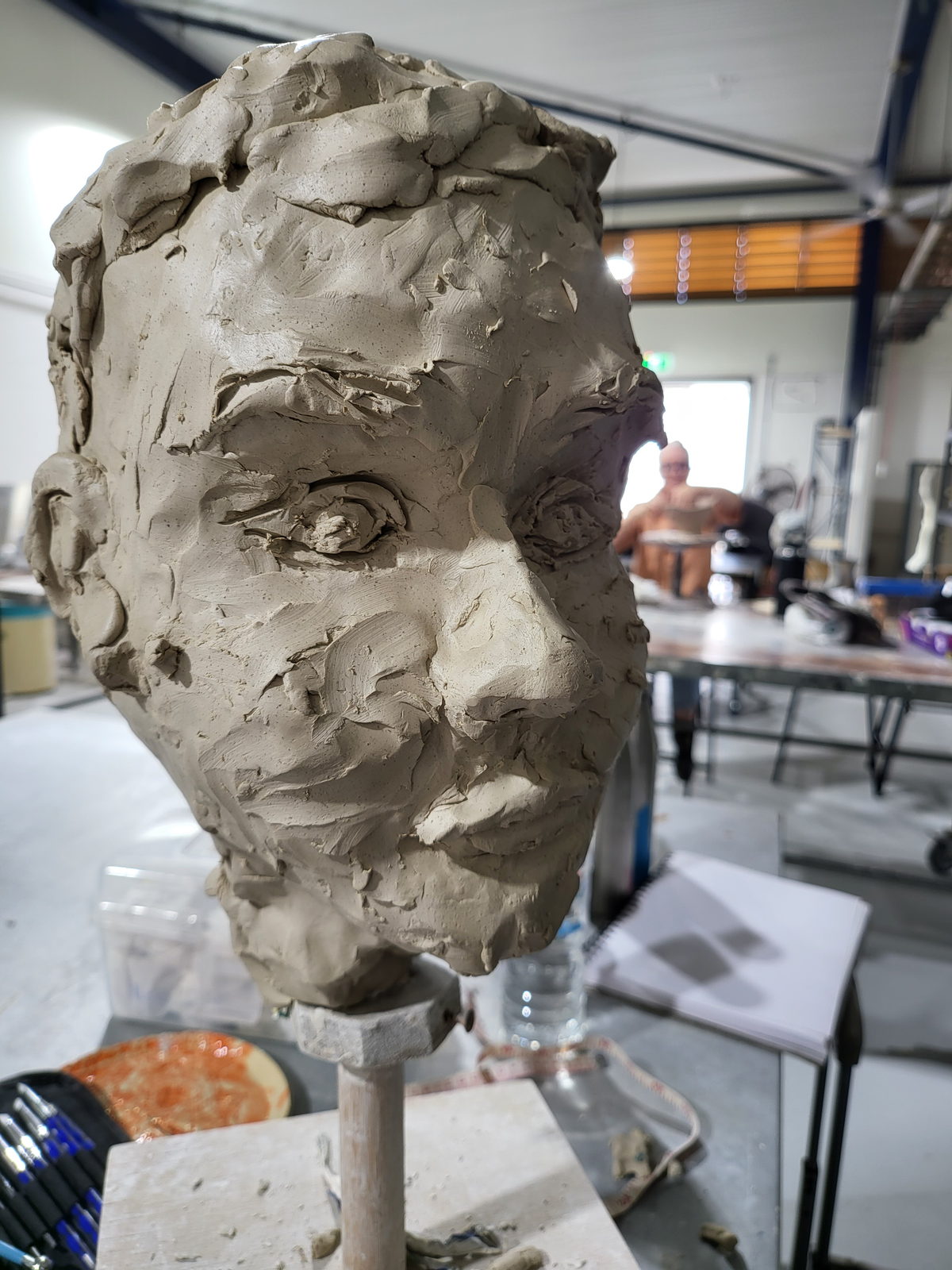 An early portrait head in grey clay on a modelling stand in the TAFE studio, roughly worked with visible tool marks